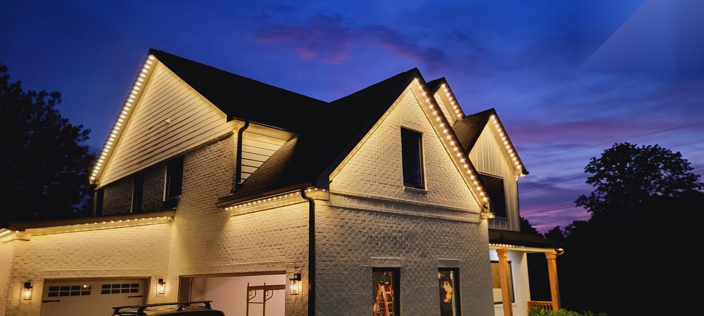 Two-story home with warm white permanent lighting along the roofline at dusk