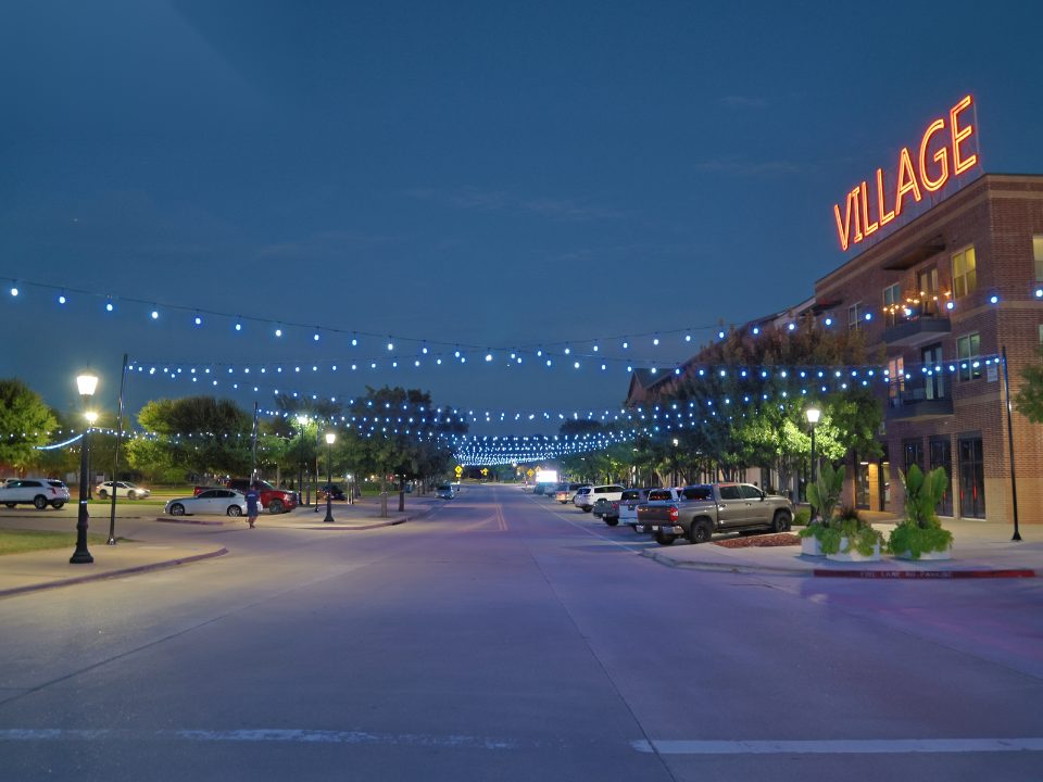 String lights spanning a street lined with trees at dusk
