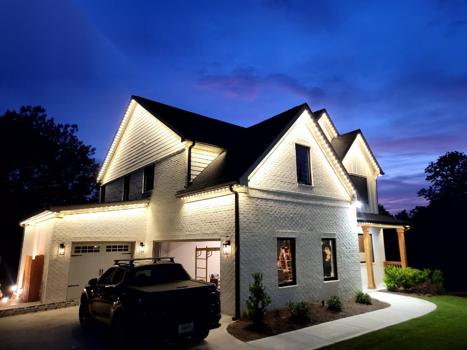 Two-story home with warm white permanent roofline lighting at dusk