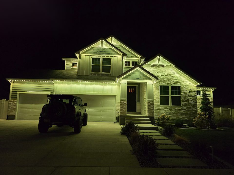 Two-story home fully washed in green permanent lighting along the roofline