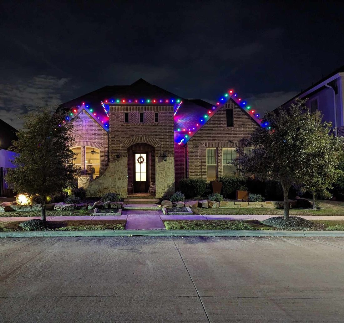 Home roofline lit in blue, red, and green for the holidays at dusk