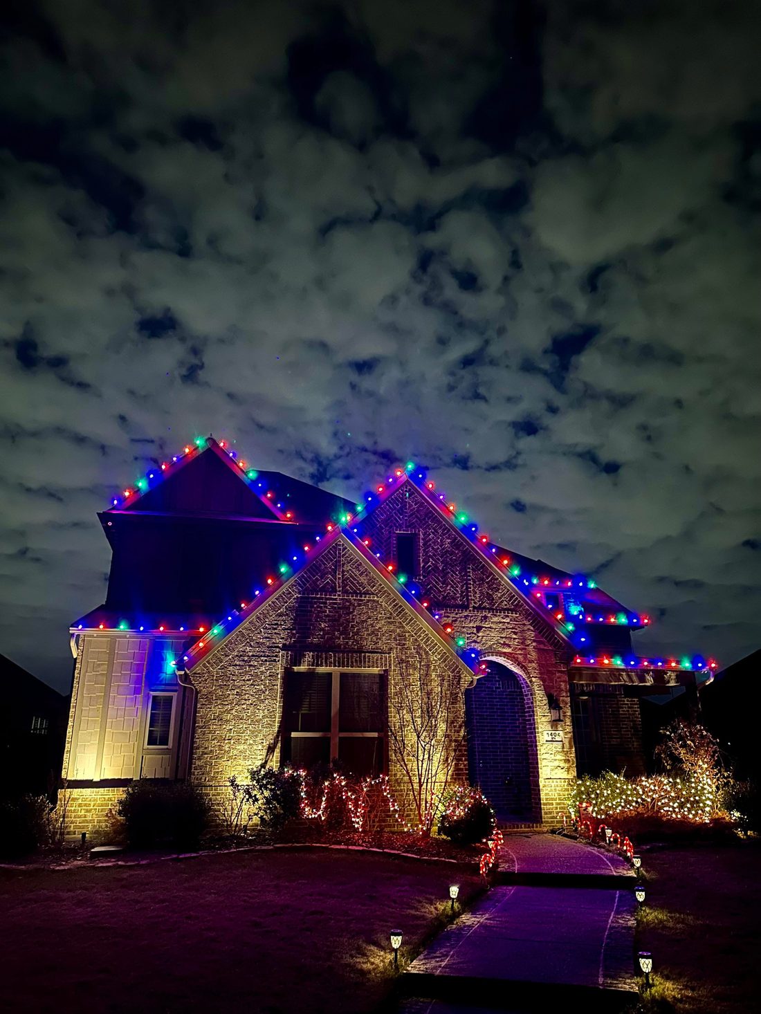 Close-up of blue, red, and green holiday roofline lighting under clouds
