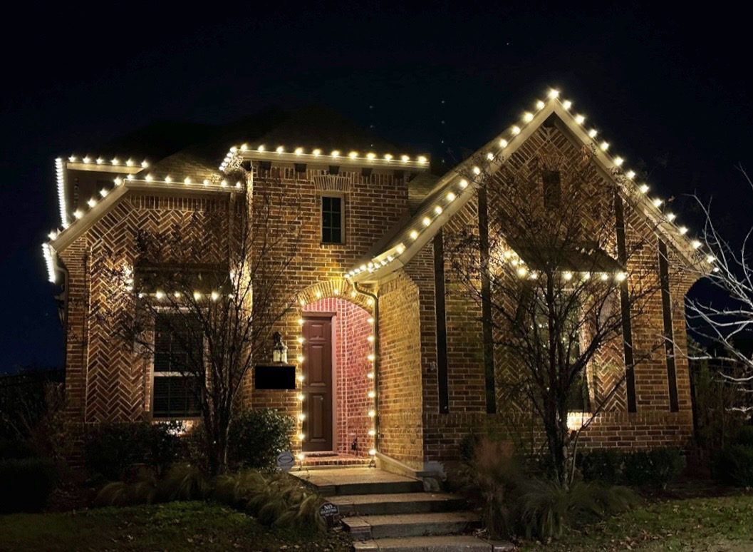 Two-story brick home with warm white holiday lighting along every roofline